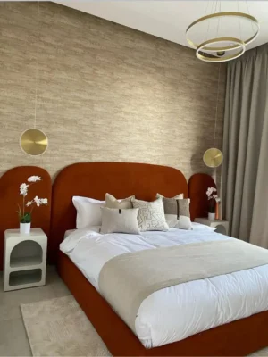 Superbe lit moderne avec une haute tête de lit arrondie en velours terracotta (orange brûlé), pour une chambre design. Ameublement Hicham Marrakech.
