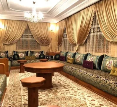 Luxueux salon marocain traditionnel avec sedari en tissu riche vert et doré, tables en bois sculpté et coussins assortis, disponible chez Ameublement Hicham à Marrakech.