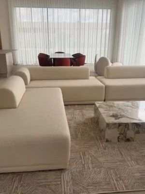 Vaste composition de salon moderne avec un canapé modulable aux formes arrondies en tissu crème, accompagné de tables basses en marbre et bois. Ameublement Hicham Marrakech.