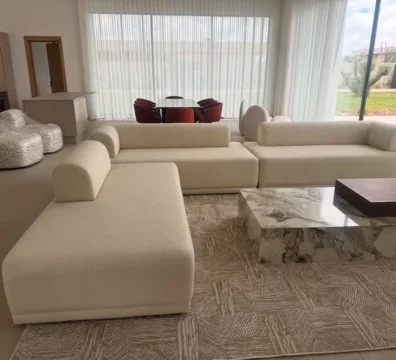 Vaste composition de salon moderne avec un canapé modulable aux formes arrondies en tissu crème, accompagné de tables basses en marbre et bois. Ameublement Hicham Marrakech.