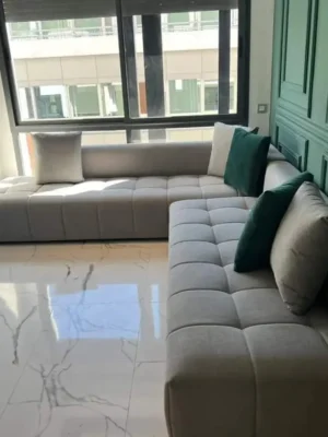 Canapé d'angle au design moderne avec un capitonnage à carrés (biscuit), en tissu gris clair, dans un salon élégant. Ameublement Hicham Marrakech.