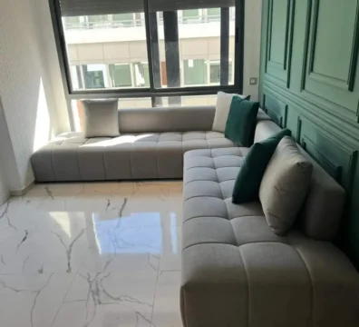 Canapé d'angle au design moderne avec un capitonnage à carrés (biscuit), en tissu gris clair, dans un salon élégant. Ameublement Hicham Marrakech.