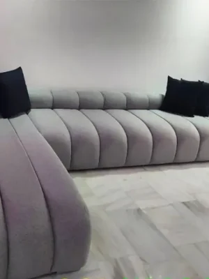 Canapé d'angle au design unique avec un capitonnage vertical tubulaire sur toute la structure, en tissu gris clair, pour un salon contemporain. Ameublement Hicham.