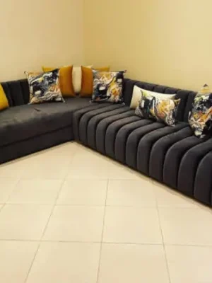 Canapé d'angle au design moderne avec un capitonnage vertical tubulaire, en velours gris anthracite, et des coussins artistiques colorés. Ameublement Hicham Marrakech.