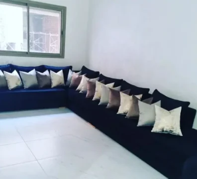 Grand canapé d'angle panoramique en velours bleu nuit, accompagné de nombreux coussins décoratifs dans une pièce lumineuse. Ameublement Hicham Marrakech.