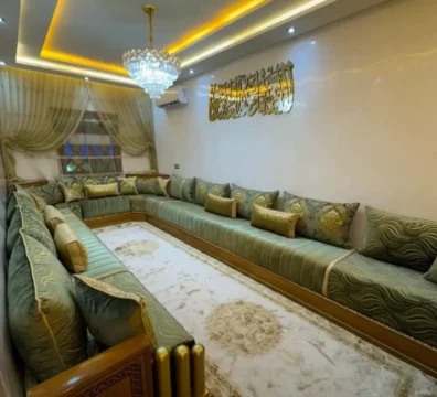 Grand salon marocain panoramique en velours vert sauge, avec des coussins dorés et une structure en bois avec finition dorée. Ameublement Hicham Marrakech.
