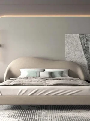 Lit design moderne avec une tête de lit incurvée et un cadre en tissu beige, posé sur de fins pieds en métal. Ameublement Hicham Marrakech.