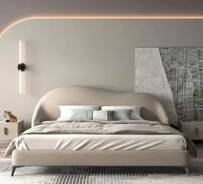 Lit design moderne avec une tête de lit incurvée et un cadre en tissu beige, posé sur de fins pieds en métal. Ameublement Hicham Marrakech.