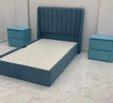 Lit simple moderne avec une tête de lit à oreilles (winged) à capitonnage vertical et des chevets assortis, en tissu bleu ciel.