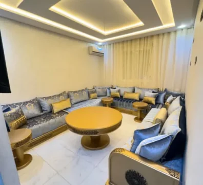 Salon marocain moderne en U avec sedari en tissu bleu et détails dorés, tables d'appoint et structure en bois doré. Ameublement Hicham Marrakech.