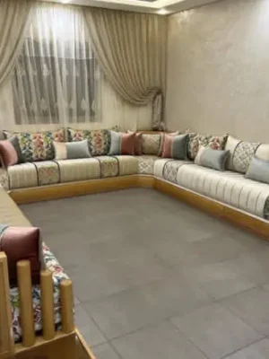 Grand salon marocain moderne en U avec une structure en bois clair, alliant un tissu uni et un tissu à motifs floraux colorés. Ameublement Hicham Marrakech.