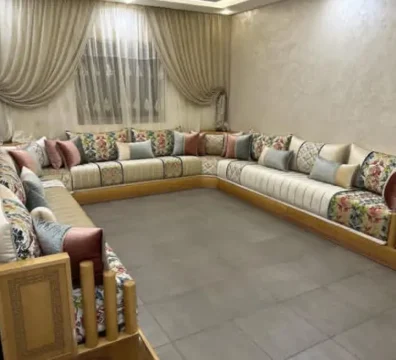 Grand salon marocain moderne en U avec une structure en bois clair, alliant un tissu uni et un tissu à motifs floraux colorés. Ameublement Hicham Marrakech.