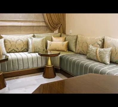 Salon marocain moderne en L, avec sedari en velours vert-gris et tissu damassé, et des tables d'appoint en bois foncé. Ameublement Hicham Marrakech.