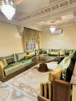 Salon marocain traditionnel en velours vert et doré avec une structure en bois sculpté, dans un intérieur richement décoré. Ameublement Hicham Marrakech.