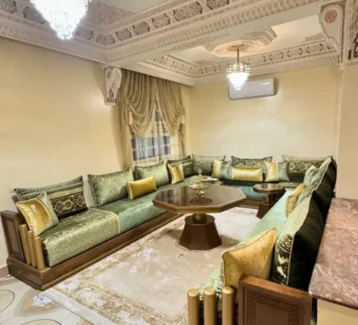 Salon marocain traditionnel en velours vert et doré avec une structure en bois sculpté, dans un intérieur richement décoré. Ameublement Hicham Marrakech.