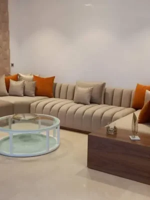 Salon moderne design en tissu beige, avec une assise à capitonnage vertical et des coussins couleur terracotta, dans un salon contemporain. Ameublement Hicham Marrakech.