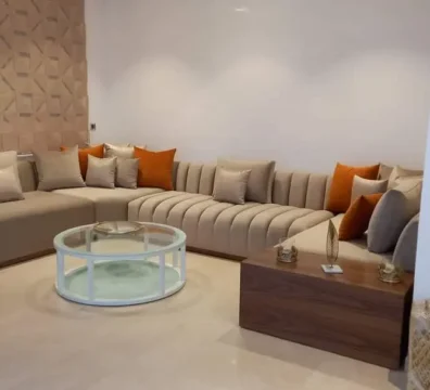 Salon moderne design en tissu beige, avec une assise à capitonnage vertical et des coussins couleur terracotta, dans un salon contemporain. Ameublement Hicham Marrakech.