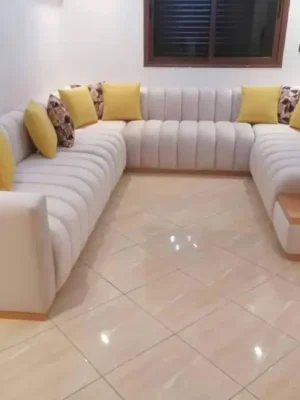 Grand salon moderne panoramique en U avec un capitonnage tubulaire, en tissu blanc cassé, rehaussé de coussins jaunes vifs. Ameublement Hicham Marrakech.